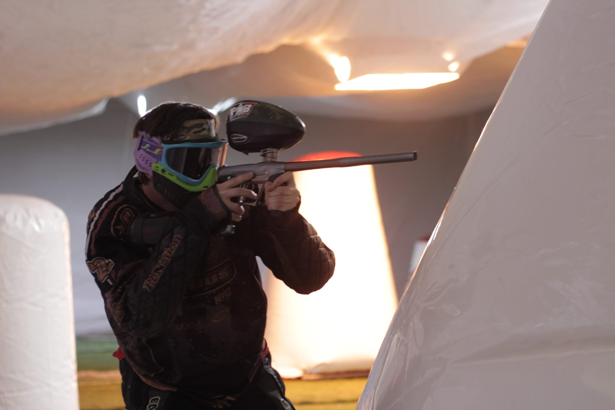 Indoor paintball player shooting from behind a barrier.