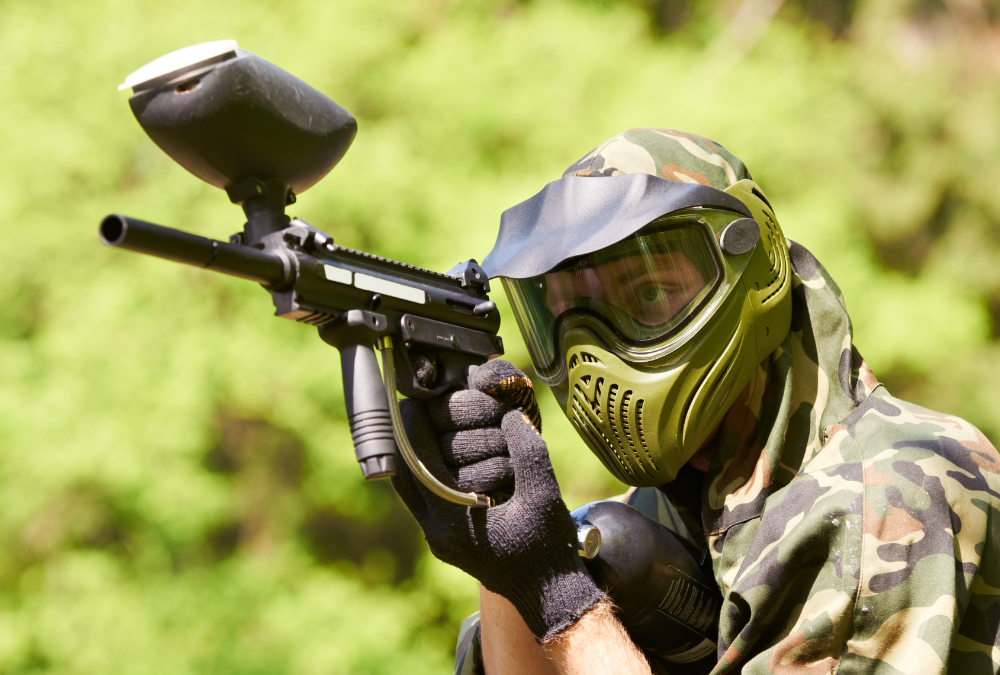 A paintball player holding a paintball gun, wearing a helmet designed specifically for paintball.