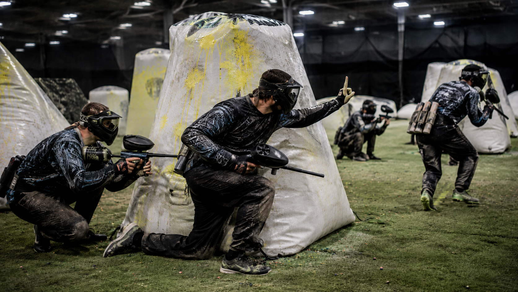 Paintball players using cover, communication, and teamwork during an indoor speedball match.